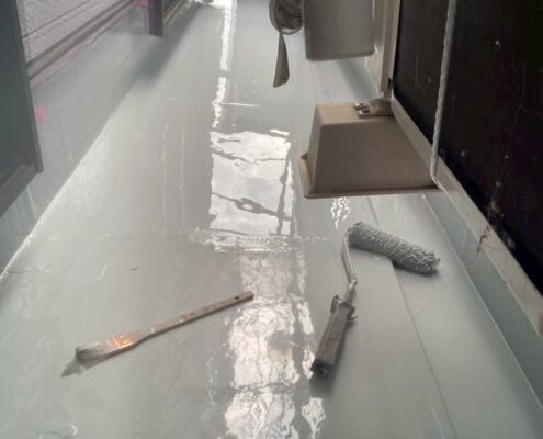 ベランダ防水工事中の様子。ウレタン防水材の2層目をローラーで丁寧に塗布し、壁際や立ち上がり部も養生された状態